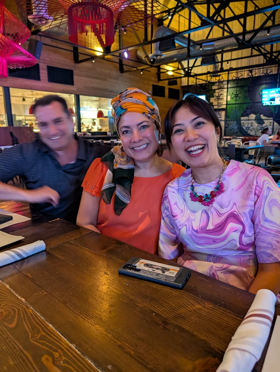 Gilbert Toastmasters members Paco, Elle, and Eunice smiling together over dinner at a restaurant