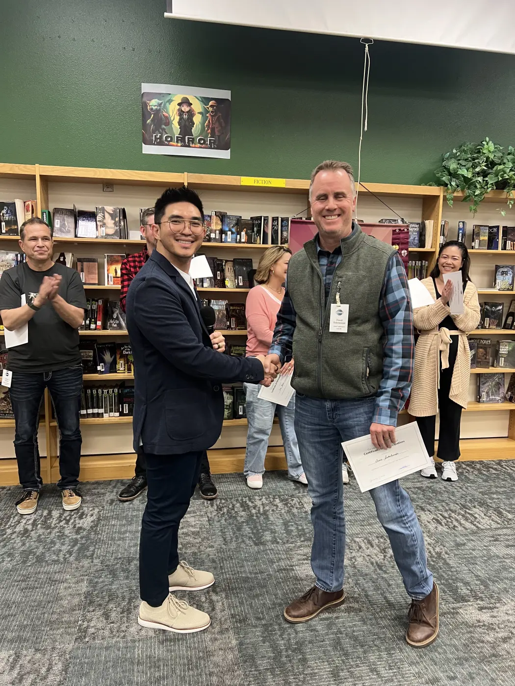 The Contest Chair shaking hands with a contestant and presenting a certificate of participation at the 2026 Gilbert Toastmasters Tall Tales contest